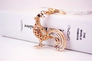 Macro detail of a golden metal rooster keychain with intricate clover cutouts on a book