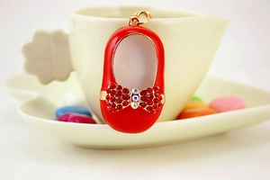 Detailed close-up of a red enamel baby shoe pendant with rhinestone bow and gold metal accents