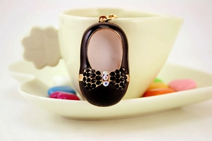 Close-up of black enamel shoe keychain with rhinestone bow on a coffee cup