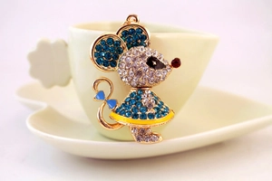 Close-up of mouse keychain with blue rhinestones and gold frame on a coffee cup edge