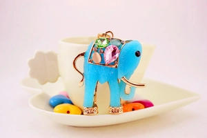 Detail of colorful resin elephant keychain with faux gemstones on white ceramic cup