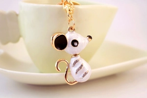 Détail d'un porte-clés souris en émail blanc et strass posé sur une tasse en céramique