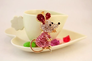 Détail d'un porte-clés souris en cristal posé contre une tasse de café couleur crème