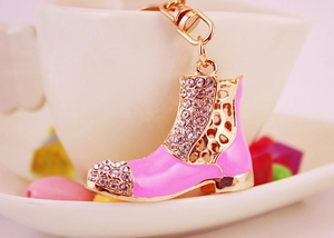 Dettaglio del portachiavi a stivale rosa con strass appeso al bordo di una tazza di porcellana