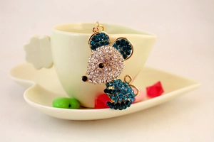 Close-up of golden mouse keychain with blue and white crystals next to a coffee cup