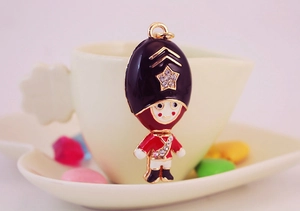 Close-up of Royal Guard keychain with red enamel and sparkling rhinestones by a coffee cup