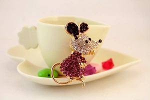 Détail d'une broche souris dorée avec cristaux violets et strass brillants sur plat
