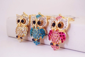 Détail de trois porte-clés hibou en strass colorés bleu, rose et blanc avec métal doré
