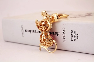 Détail d'un porte-clés souris dorée avec cœurs évidés et strass roses sur un livre blanc