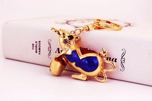 Detail of a golden mouse keychain with blue and red enamel patterns on a white book
