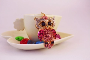 Détail d'un porte-clés chouette coloré en strass suspendu à une tasse de café blanche