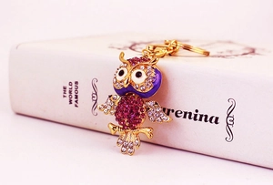 Close-up of golden owl keychain with pink and purple rhinestones on a book background