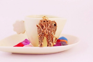 Close-up of golden elephant keychain pendant with amber rhinestones near a white cup