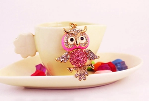 Close-up of pink rhinestone owl keychain hanging on a white ceramic cup edge