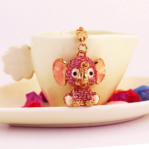 Cute pink rhinestone elephant keychain with gold accents on a white decorative ceramic cup