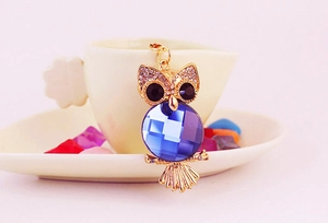 Détail du porte-clés hibou avec cristal bleu et métal doré accroché à une tasse blanche