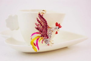 Macro detail of rooster keychain with colorful rhinestones on a white coffee cup rim