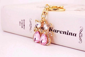 Detailansicht zweier goldener Katzen-Schlüsselanhänger mit rosa und weißen Kristallen