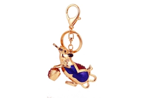 Detailed close-up of golden mouse keychain with blue enamel and coin pattern on white background