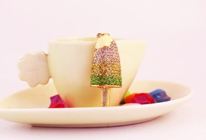 Close-up of a colorful popsicle charm with rhinestones hanging on a ceramic cup edge