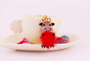 Close-up of a cartoon cow keychain featuring a red pompom and rhinestones on a cup