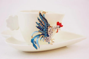 Detailed view of rooster keychain with blue rhinestones hanging on a white ceramic cup