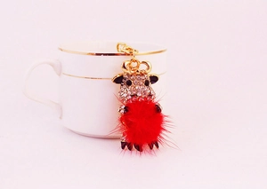 Close-up of a cartoon cow keychain with red pompom and rhinestones on a white coffee cup