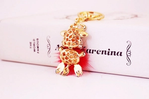 Detail of golden plated ox keychain featuring lucky clover cutout and red plush ball charm