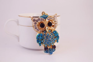 Détails d'un pendentif hibou doré orné de strass bleus et blancs sur une tasse chic