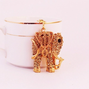 Golden elephant keychain with sparkling yellow rhinestones hanging on a white ceramic cup
