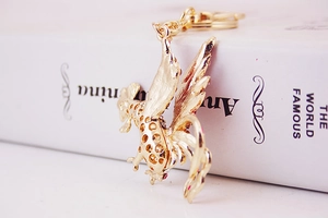Macro shot of gold rooster keychain with pink rhinestones on a white book edge