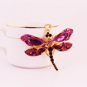 Porte-clés libellule doré avec cristaux violets posé sur une tasse à café blanche