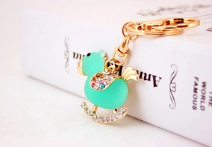 Macro shot of mint green crystal rocking horse keychain with gold hardware on book
