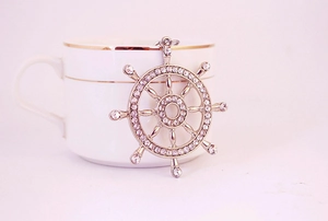 Détail d'un pendentif gouvernail en argent serti de strass brillants sur une tasse en porcelaine