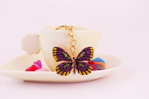 Detail of colorful rhinestone butterfly keychain with gold lobster clasp on white saucer