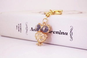 Detailed close-up of a golden owl keychain featuring yellow enamel and purple gem eyes