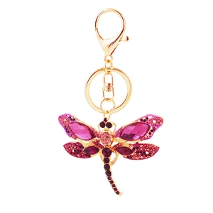 Porte-clés libellule doré orné de cristaux magenta et strass sur fond blanc éclatant