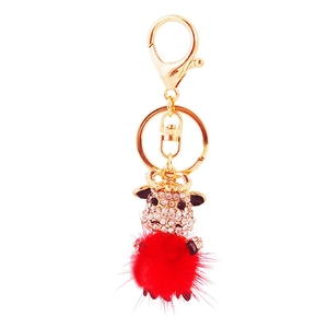 Cartoon cow keychain with red faux fur pompom and crystal rhinestones on white background