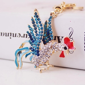 Golden rooster keychain with sparkling rhinestones and blue enamel feathers on white books