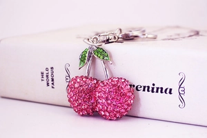 Detailed macro view of sparkling pink and green rhinestone cherry keychain on a white book