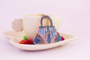 Detail of a handbag-shaped keychain with pink and blue rhinestones on a coffee cup
