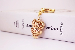 Close-up of golden owl keychain with hollow metal design leaning on a white book