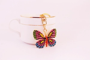 Detail of a butterfly keychain with colorful rhinestones hanging on a white ceramic cup