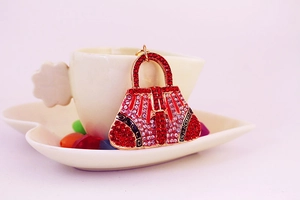 Detailed close-up of a luxury red handbag keychain with sparkling rhinestones on a white cup