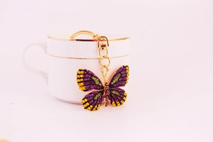 Detail of colorful rhinestone butterfly keychain with gold lobster clasp on white cup
