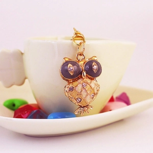 Sparkling crystal owl keychain with purple rhinestones on a decorative ceramic saucer