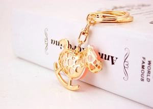 Close-up of golden rocking horse keychain with hollow heart pattern on white book