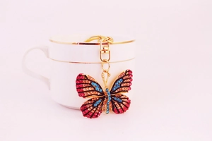 Close-up of a colorful rhinestone butterfly keychain on a white porcelain cup