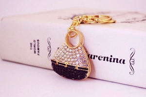 Close-up of a gold alloy bag-shaped keychain featuring white and black rhinestones