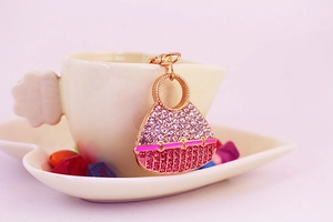 Close-up of pink and purple crystal handbag keychain with gold metal clasp on porcelain